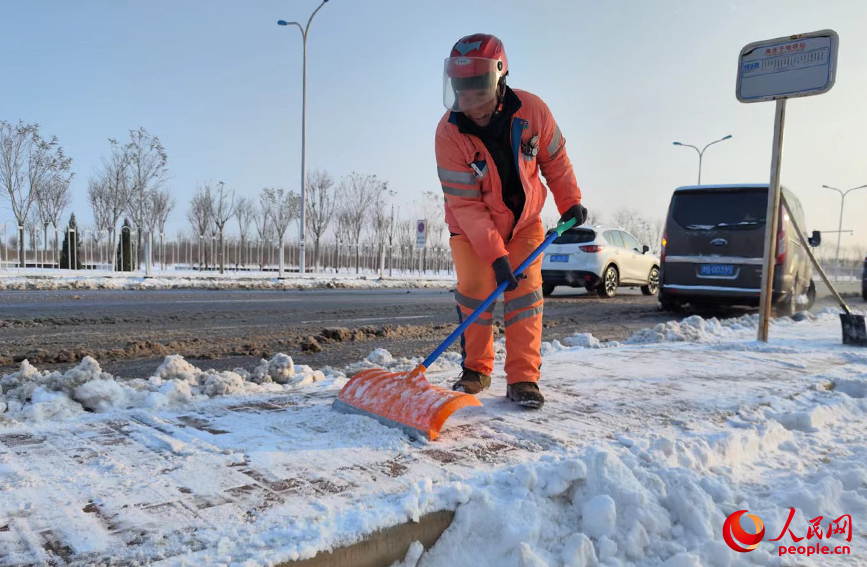 公交站邊，環衛工人手持推雪板，為市民掃出“平安路”，創造安全的通行環境。人民網 郭維瑾攝