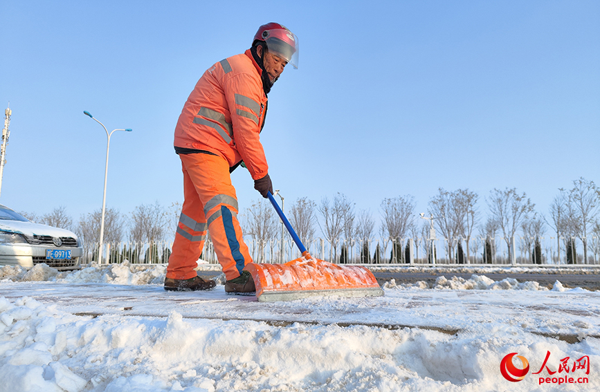 环卫工人手持推雪板，清扫便道上的积雪，守护市民出行“平安路”。人民网 郭维瑾摄