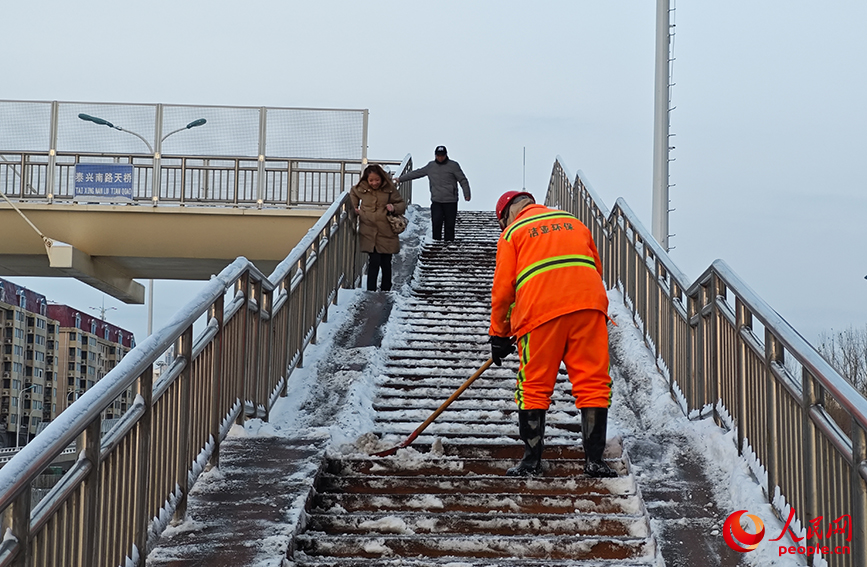 天津市河东区泰兴南路天桥上，环卫工人正在清理桥面积雪，行人小心翼翼地下桥。人民网记者 孙一凡摄