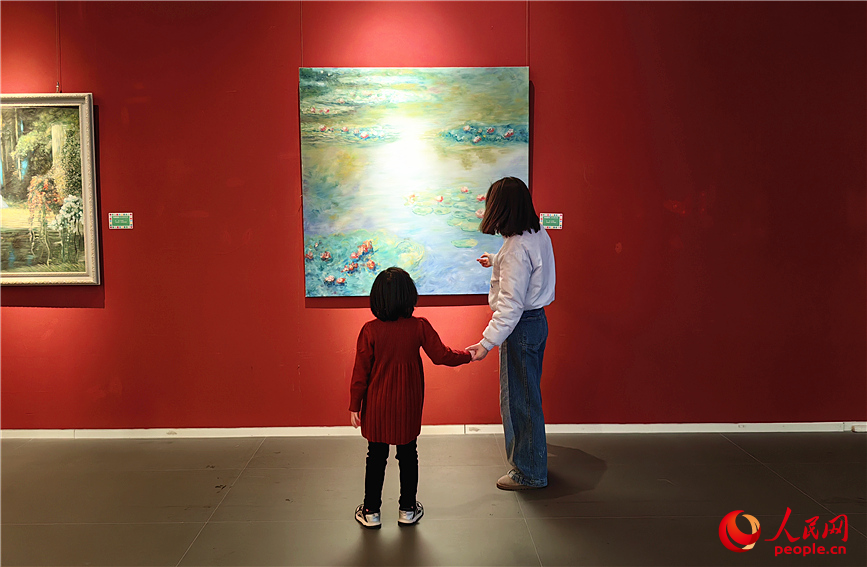 一位小女孩与母亲并肩站在一幅画作前，轻声讨论。人民网记者 李丹摄